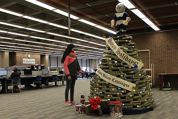 A student admires a holiday tree made of volumes stacked by the Leddy Library’s resident elves.