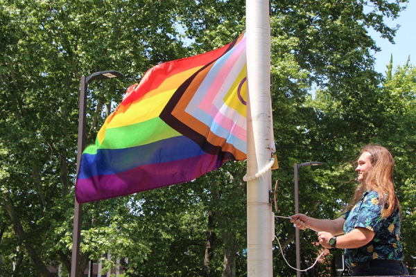 Mack Park pulls on rope to raise Progress Pride banner up flagpole.