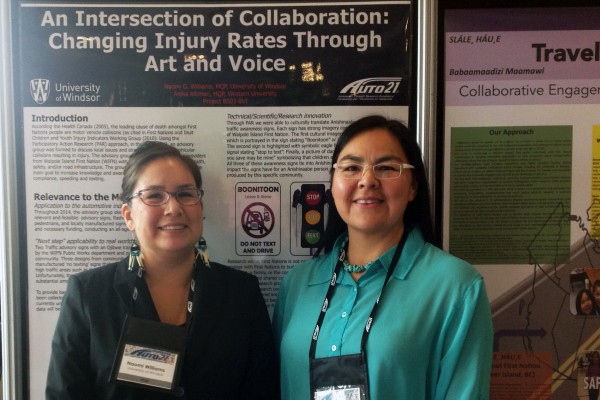 UWindsor PhD student Naomi G. Williams (l.) and research partner Anika Altiman (r.) pose with their poster tailored to incorporate Indigenous languages and art in a campaign to reduce the risk of vehicular injury among Indigenous people in Walpole Island 