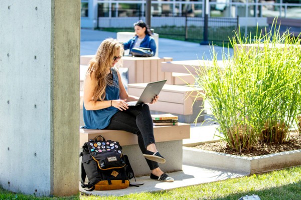 A University of Student works outside on her laptop. 